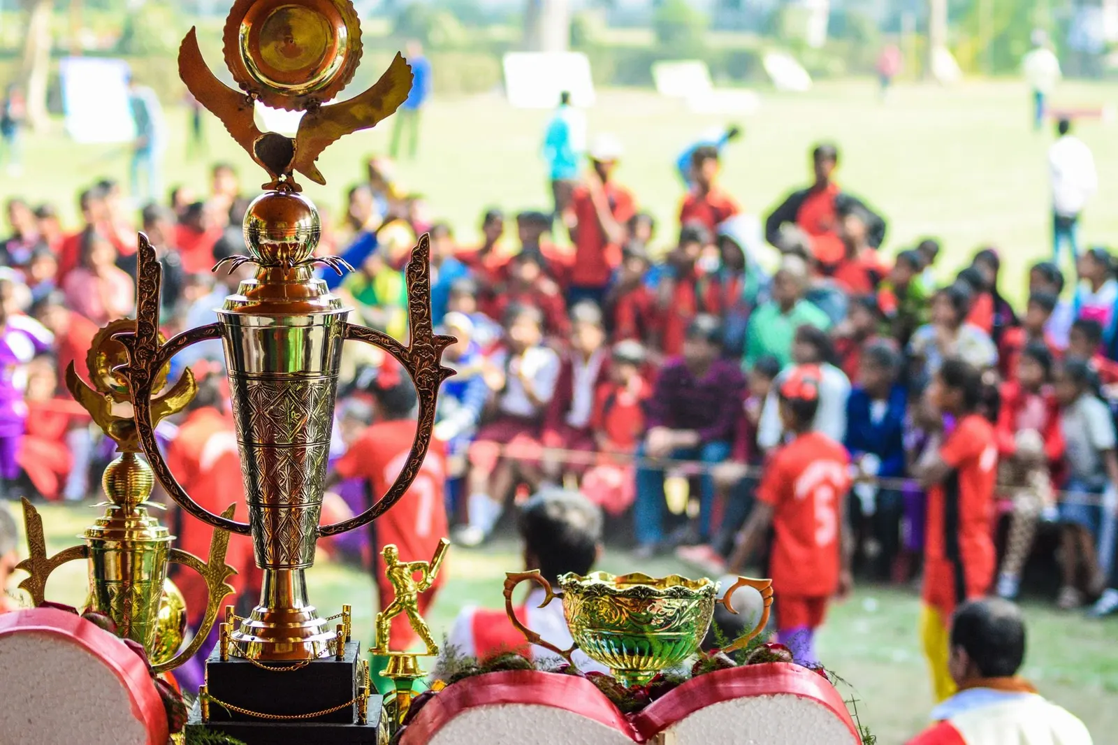 Trophies lined up at a Friends of Calcutta sports tournament, with the crowd behind